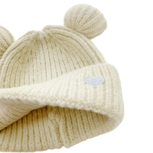 Detail of cream knit beanie featuring bear ears and a white heart embroidery patch
