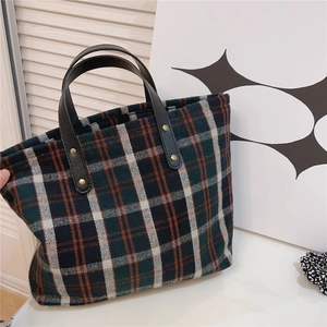 Close-up of plaid canvas tote with leather handles and gold rivet reinforcements