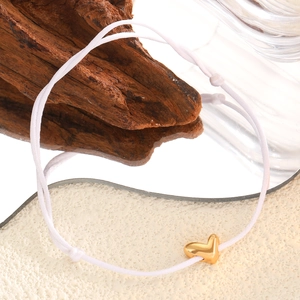 Détail d'un bracelet en corde tressée blanche avec un pendentif en forme de cœur doré