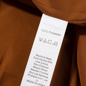 Detailansicht der 100% Polyester-Stoffstruktur und des Pflegeetiketts für den Karo-Mantel