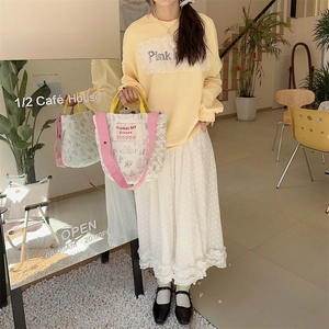 Détail du sac seau matelassé à fleurs avec poignée jaune et sangle rose au café