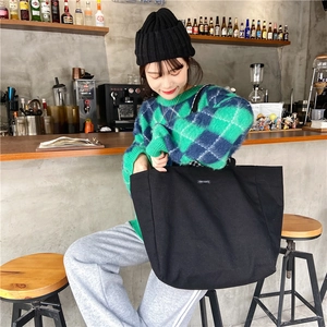 Lifestyle shot of large black canvas tote bag with brand label in a cafe setting