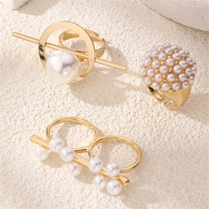 Three-piece gold-finished rings set featuring white pearls on a textured background