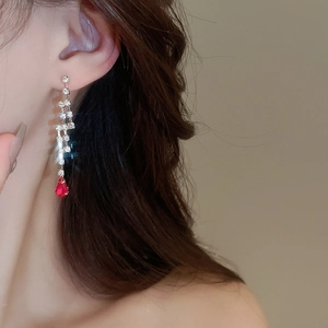 Detail of silver drop earrings with white diamonds and red teardrop gemstones on a model