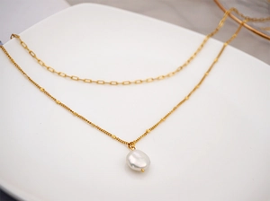 Detailed view of gold double-layer necklace with baroque pearl and rectangular links