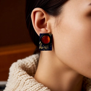 Close-up of model wearing dark blue resin square earrings with golden texture and amber center