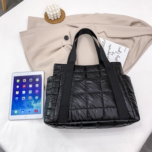 Modern black quilted tote bag made of shiny nylon fabric shown with a tablet and blazer