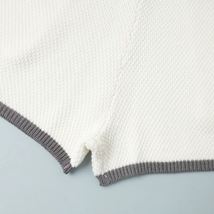 Detailed close-up of white knit top featuring grey ribbed hem and refined side slit detail