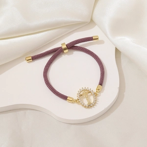 Dettaglio del bracciale in corda intrecciata viola con ciondolo a croce d'oro su seta