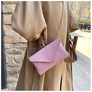 Detail of a pink suede envelope crossbody bag with a slim metal chain strap on a model