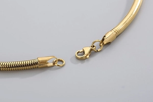Détail d'un collier chaîne serpent dorée mettant en valeur le fermoir mousqueton