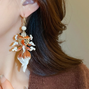 Macro detail of goldfish enamel earrings with pearl accents on a female model