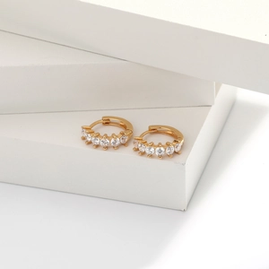 Close-up of gold hoop earrings with five white zircons on minimalist white blocks