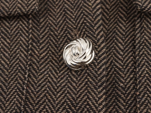 Détail macro du tissu en tweed à chevrons marron avec un bouton en métal argenté