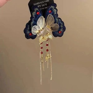 Detail of blue embroidery butterfly earrings with gold tassels and red gemstones