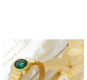 Close-up of golden textured rings with green and white gemstones on a white cloth bag