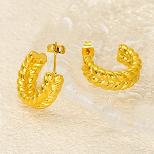 Vue rapprochée des boucles d'oreilles créoles dorées torsadées sur un fond texturé