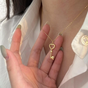 Close-up of a gold heart key pendant necklace worn on a white shirt background