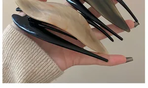Close-up of a pair of large acetate hair clips in beige marble and translucent grey finishes