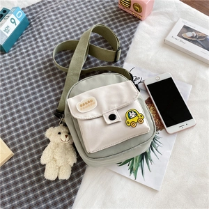 Détail du sac bandoulière en toile vert clair avec poche blanche et ours en peluche