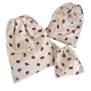 Three sizes of cream corduroy drawstring pouches with red strawberry patterns for storage