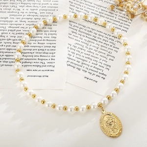 Détail de la médaille Saint Christophe sur collier de perles blanches et perles d'or