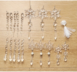 Flat lay of 18 clear acrylic snowflake and icicle ornaments on light wood with white ribbon