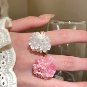 Close-up of handmade beaded flower rings in pink and white on hand with lace background