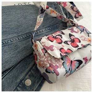 Close-up of white crossbody bag with butterfly prints resting on denim fabric