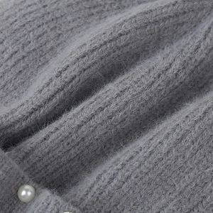 Close-up of gray chunky knit hat fabric with soft faux fur texture and a pearl button