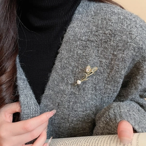 Detailed close-up of a 14K gold-plated tulip brooch with a pearl on a grey knit sweater