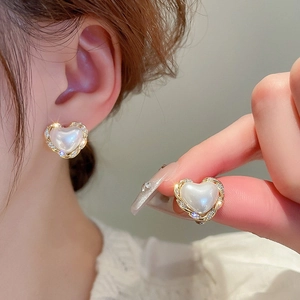 Macro detail of heart-shaped pearl earrings with gold twisted edges and sparkling crystals