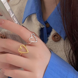 Close-up of minimalist gold and silver heart-shaped open rings worn on a person's fingers