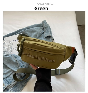 Detail of olive green canvas sling bag with embroidered letters and orange brand label