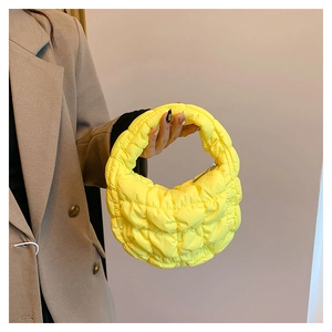 Detail view of a yellow quilted puffer handbag held by a model in a camel blazer suit