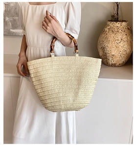 Detail of hand-woven straw tote bag with natural bamboo handles and woven texture