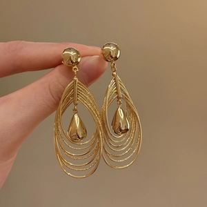 Detail view of 18k gold plated multi-layer hollow teardrop earrings held by hand