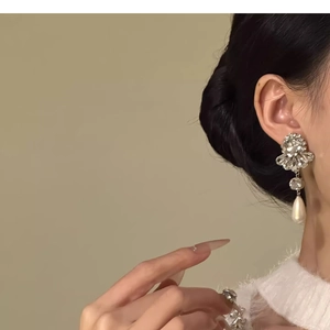 Close-up of floral rhinestone stud earring with teardrop pearl pendant on a model