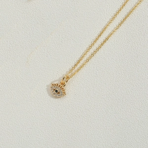 Detailed view of gold Evil Eye pendant necklace with sparkling cubic zirconia and black gemstone