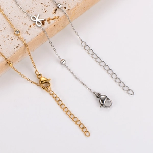 Detail view of gold and silver bow foot anklets with lobster clasps on stone background