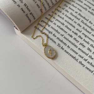 Detail of golden tulip relief on oval shell pendant resting on an open book