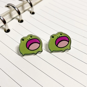 Close-up of cute green acrylic frog stud earrings with open mouth on notebook paper