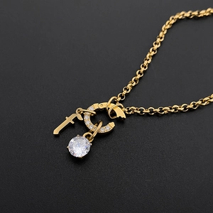 Gros plan d'un collier en acier titane doré avec lettre f et breloques en zircon.