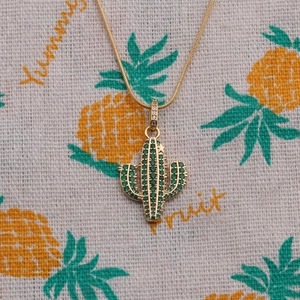 Gold cactus pendant necklace with green and white zircons on a decorative fabric background