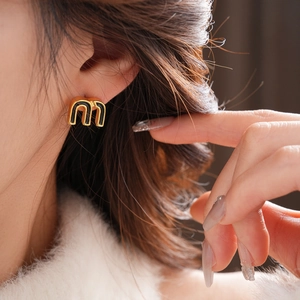 Close-up of golden letter M earrings with black enamel inlay worn on earlobe