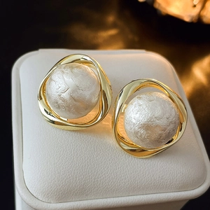 Elegant gold geometric earrings featuring textured imitation pearls on a white leather pad