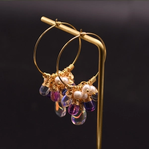 Detail of gold hoop earrings with white pearls and colorful teardrop gemstones