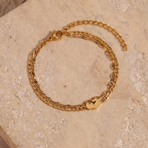 Close-up of golden double-layer chain bracelet featuring a dainty footprint pendant on stone