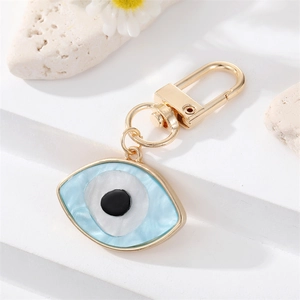 Golden Evil Eye keychain with blue marble texture on white stone background