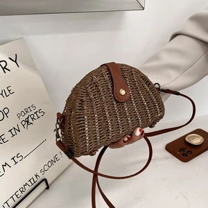 Detail of a brown woven straw crossbody bag with leather strap and metal buckle closure